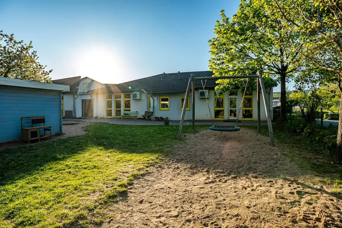 Außenbereich der Kita Schweich mit Nestschaukel und Sandfläche in der Morgensonne
