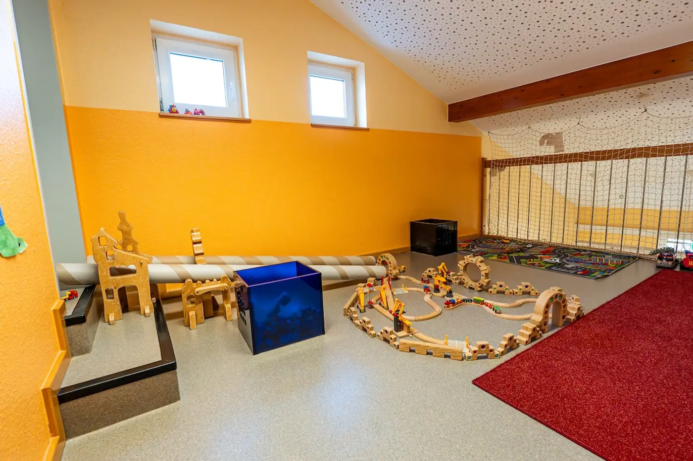 Gemütlicher Spielraum der Nestgruppe mit Holzeisenbahn und rotem Teppich in der Kita Schweich