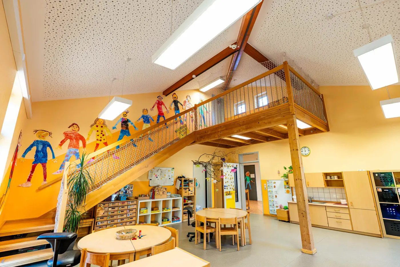 Heller Gruppenraum mit Holz-Hochebene und gemalten Kinderfiguren in der Kindertagesstätte Schweich