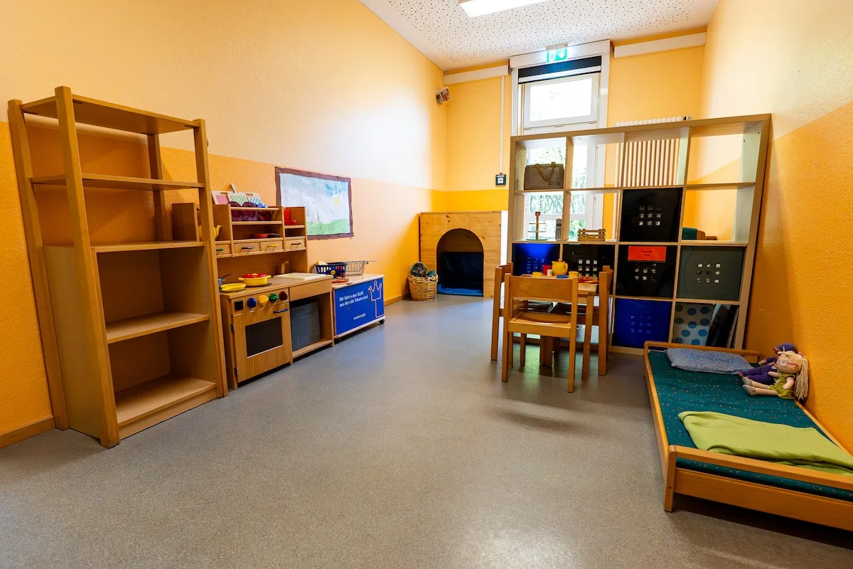 Kreativwerkstatt der Kita Schweich mit Spielküche, Holzregalen, Kindertischen und Kuschelecke in einem warm gelben Gruppenraum