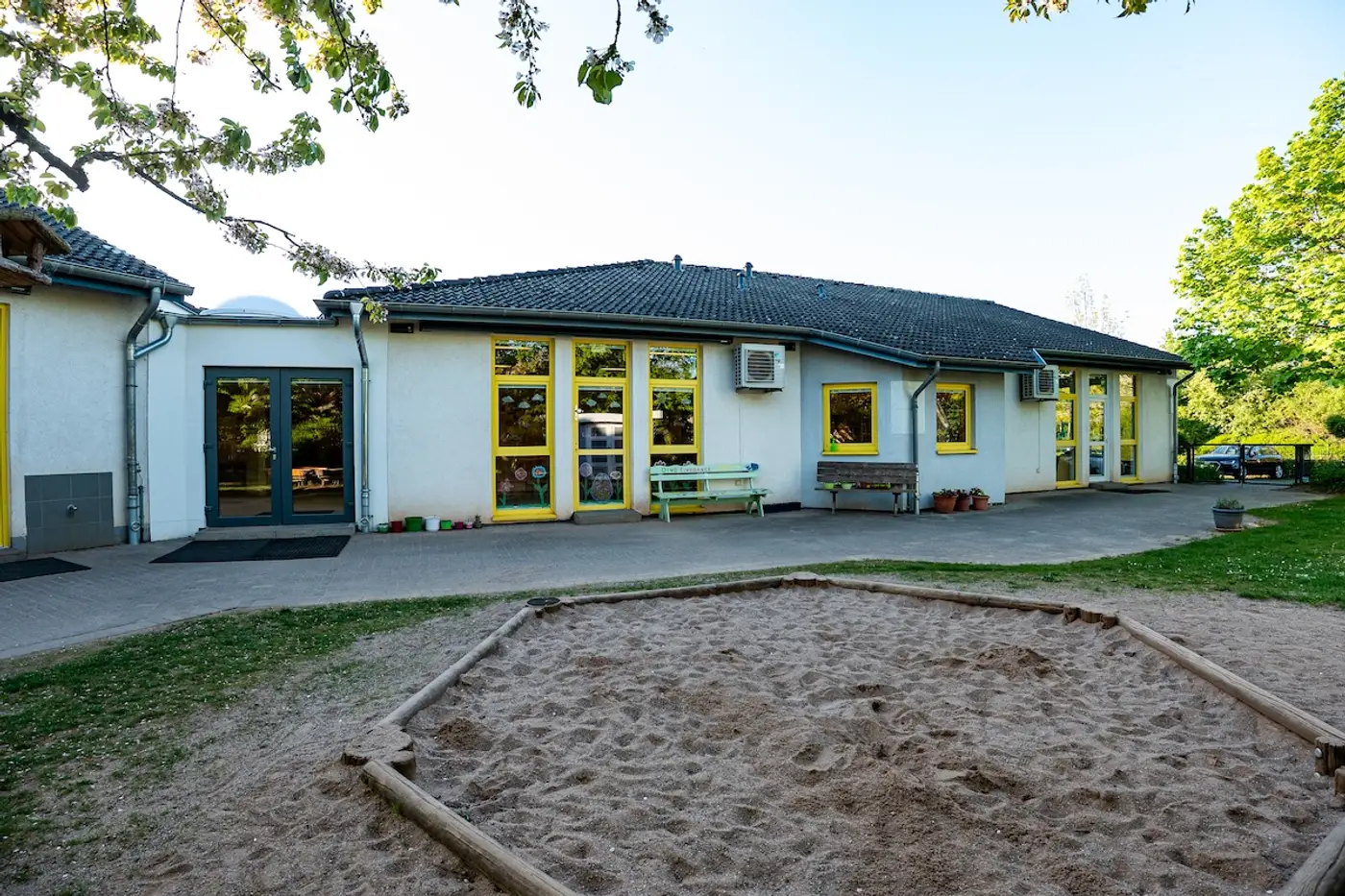 Großer Sandkasten im Innenhof der Kita Schweich mit Sitzbänken vor dem Gebäude